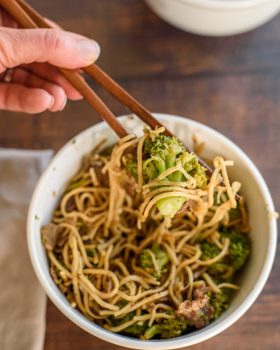 broccoli and beef with noodles in a bowl with chopsticks picking up some