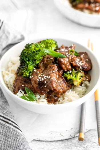 Instant Pot Mongolian Beef in a bowl with broccoli, served over rice and garnished with sesame seeds and green onions