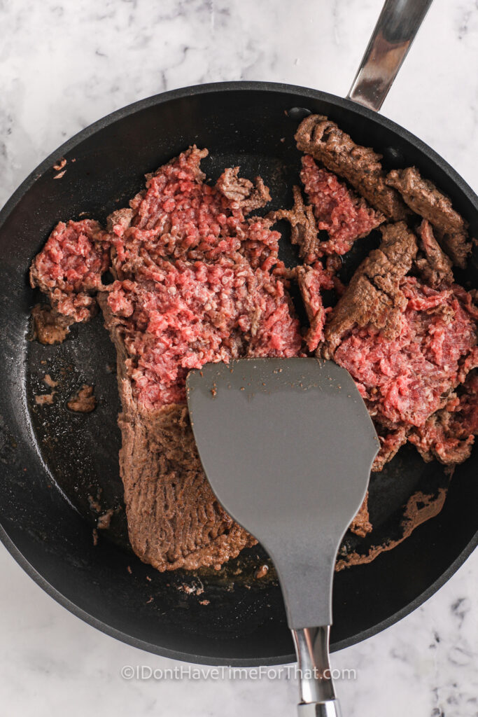 breaking ground beef into pieces in the pan to show How to Brown Ground Beef from Frozen