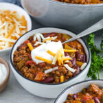 a bowl of chili with sour cream and shredded cheese on top.