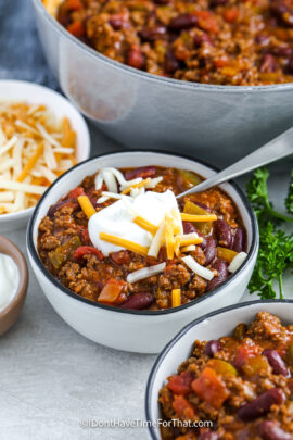 a bowl of chili with sour cream and shredded cheese on top.